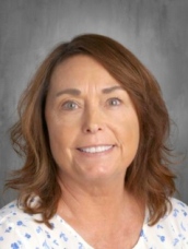 Smiling woman with shoulder-length brown hair, wearing a floral blouse, against a gray background.