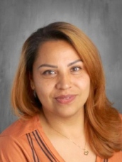 Smiling woman with long, wavy hair wearing an orange top, posed against a gray background.