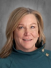 A woman with shoulder-length blonde hair smiles, wearing a teal sweater. Background features a light gray texture.