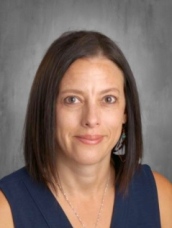 Portrait of a woman with shoulder-length brown hair, wearing a navy top, against a gray background.