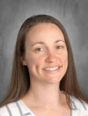Smiling woman with long brown hair wearing a striped shirt, set against a neutral background.