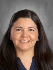 A smiling woman with long dark hair, wearing a blue top, against a gray background.