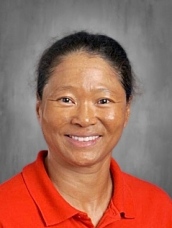 Smiling woman with dark hair wearing a red polo shirt, set against a gray background.