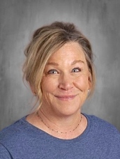 Smiling woman with light brown hair in a blue shirt, set against a gray background.