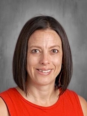 A woman with shoulder-length brown hair smiles, wearing a red top against a gray background.