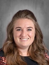 Smiling woman with long brown hair, wearing a floral blouse, against a gray background.