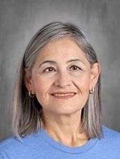 Smiling woman with shoulder-length gray hair, wearing a blue shirt, against a neutral background.
