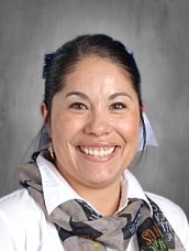 Smiling woman with dark hair, wearing a white shirt and patterned scarf, against a gray background.