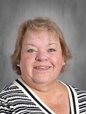 Smiling woman with short, light brown hair wearing a striped black and white top, against a gray background.