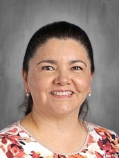 A woman with dark hair, smiling, wearing a floral blouse, set against a neutral background.